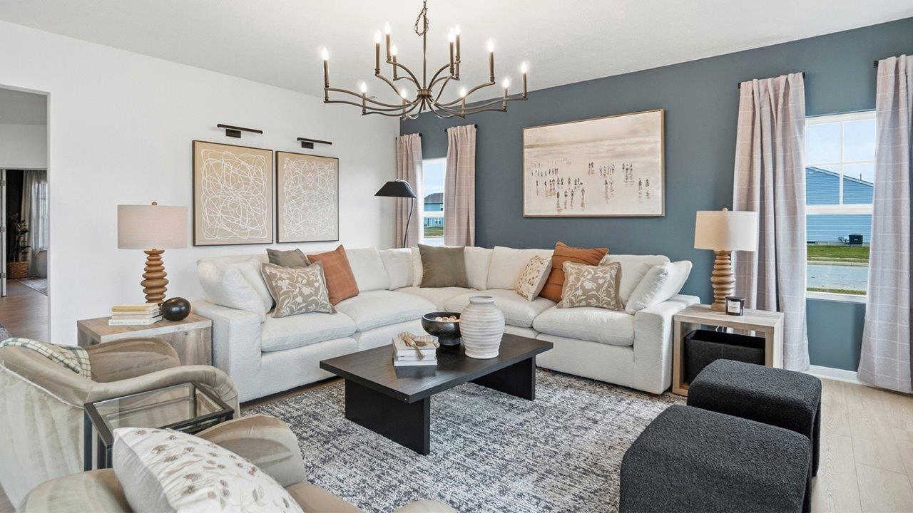 Open living area with a white sectional, beige chairs, black coffee table, patterned rug, dining table, and kitchen in the background.