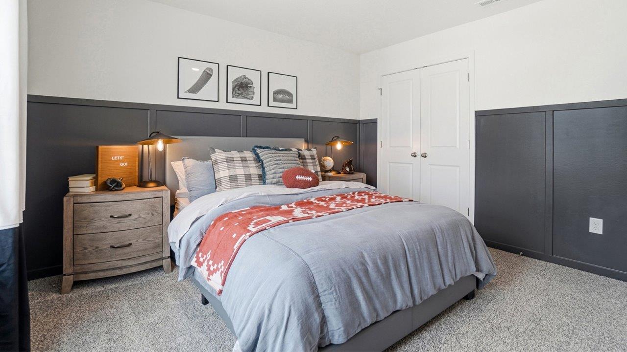 Gray upholstered bed with patterned red throw, flanked by wood nightstands against a dark paneled accent wall.