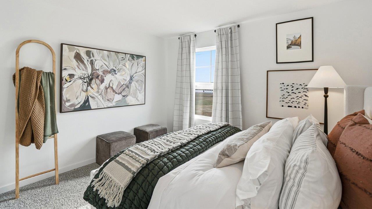 Side view of a bright bedroom with white bedding, dark green throw, floral wall art, garment rack, and window.