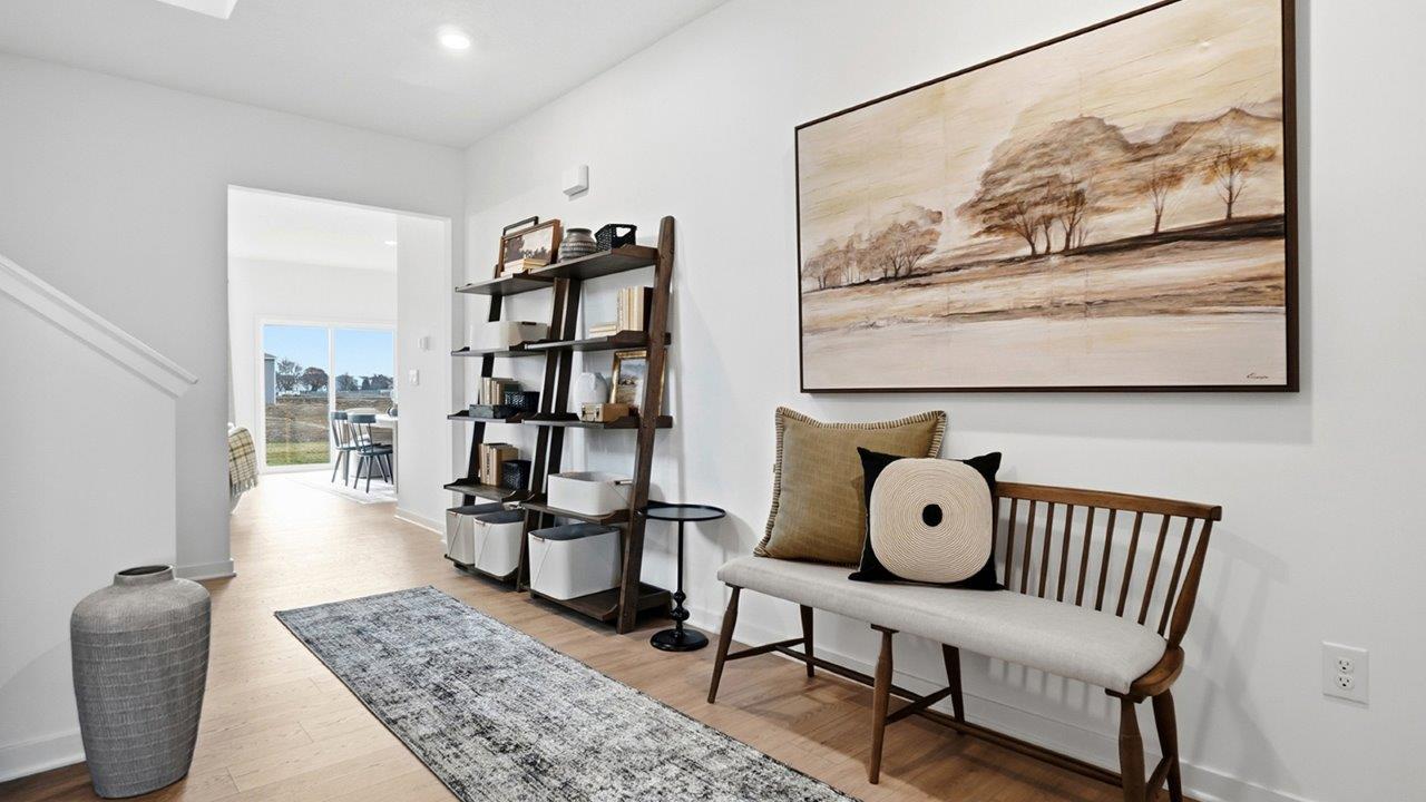 Open entry hall with a cushioned wood bench, landscape artwork, shelving unit, patterned runner, and staircase.