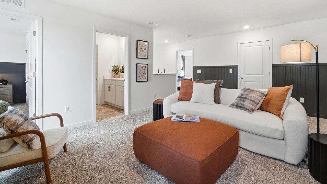 Loft sitting area with white sofa, large orange ottoman, accent chair, floor lamp, and doorways to nearby rooms.