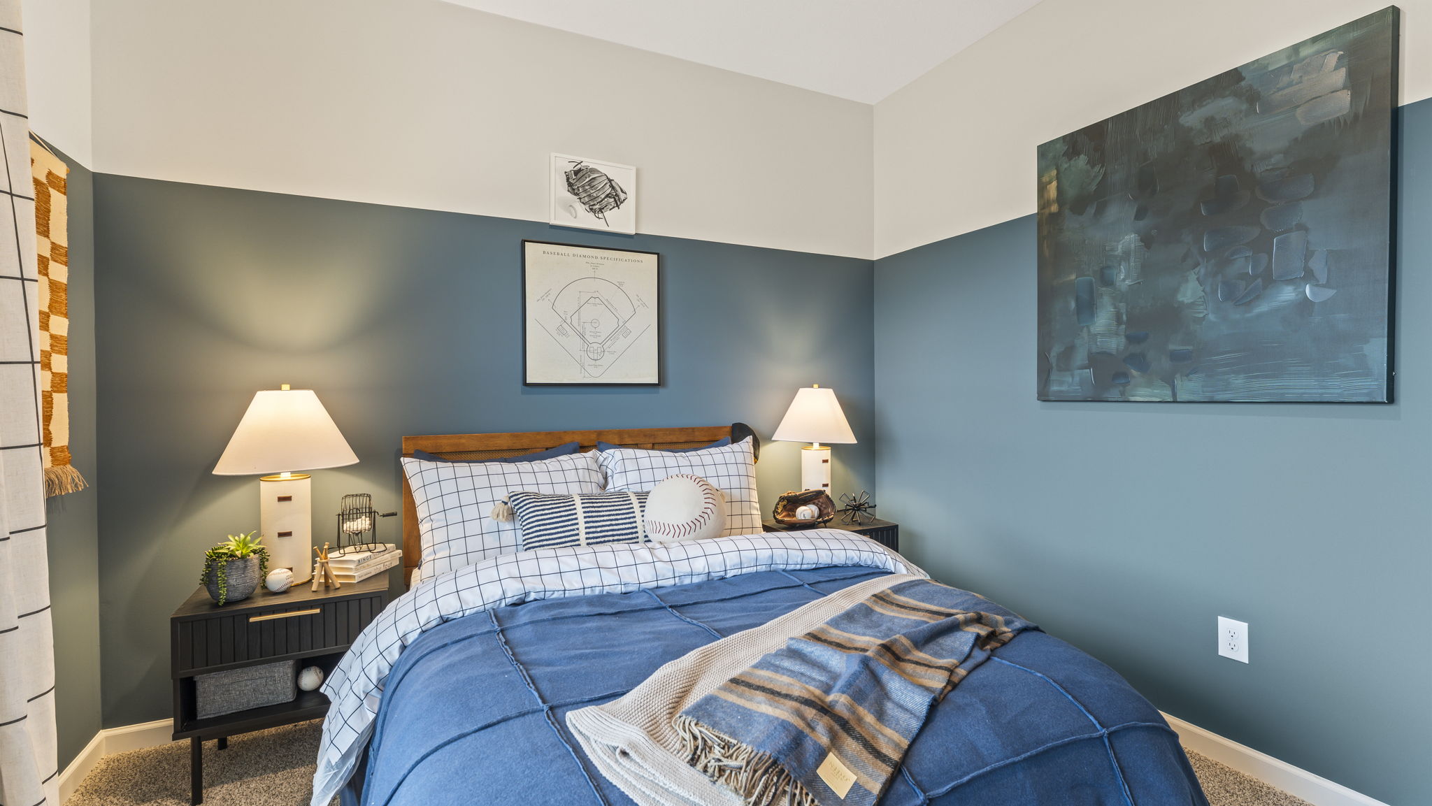 Three-quarter view of baseball-themed bedroom with blue bedding, two-tone walls, and large abstract art piece.