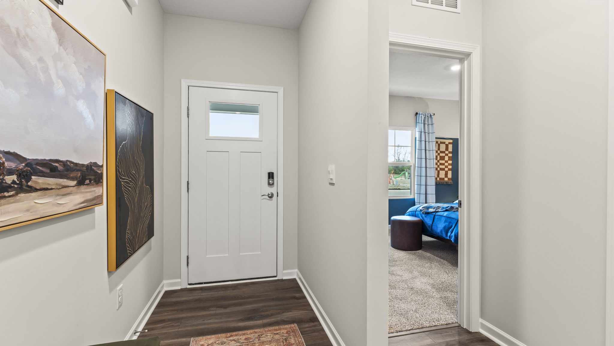 Hallway at the front of the home with door to outside on the left and view of bedroom on the right.