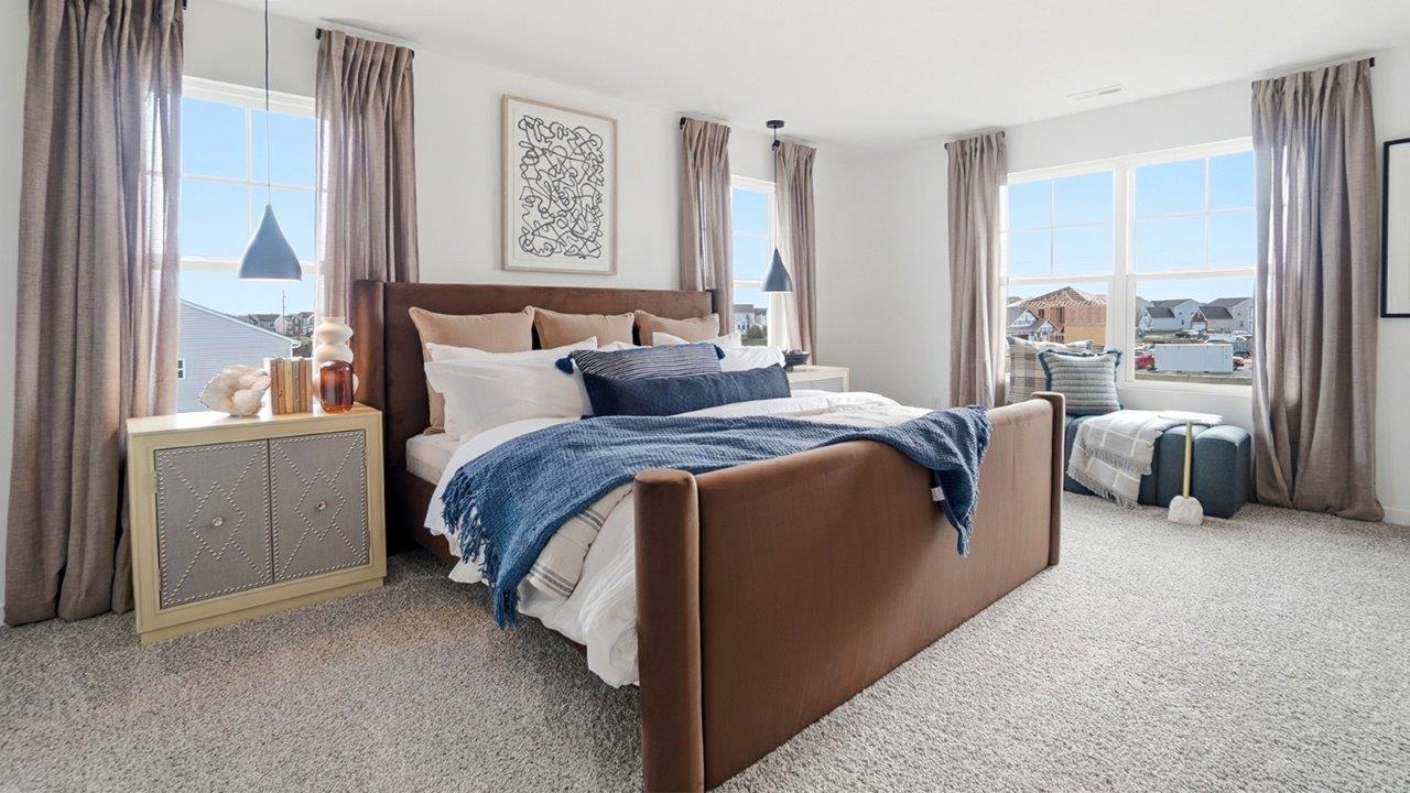 Living room with a white sectional, two beige chairs, black coffee table, fireplace, wall-mounted television, and large windows.