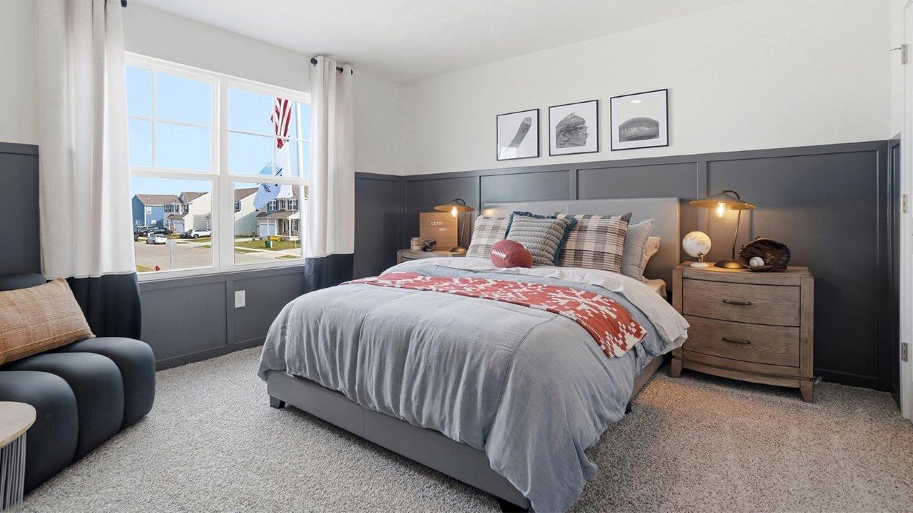 Spacious bedroom with a gray upholstered bed, dark paneled accent wall, matching nightstands, and a large window.