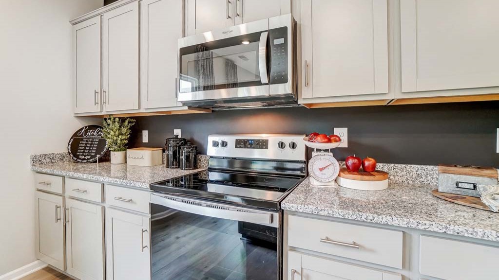 Close up of kitchen appliances and granite countertops with gray cabinets.