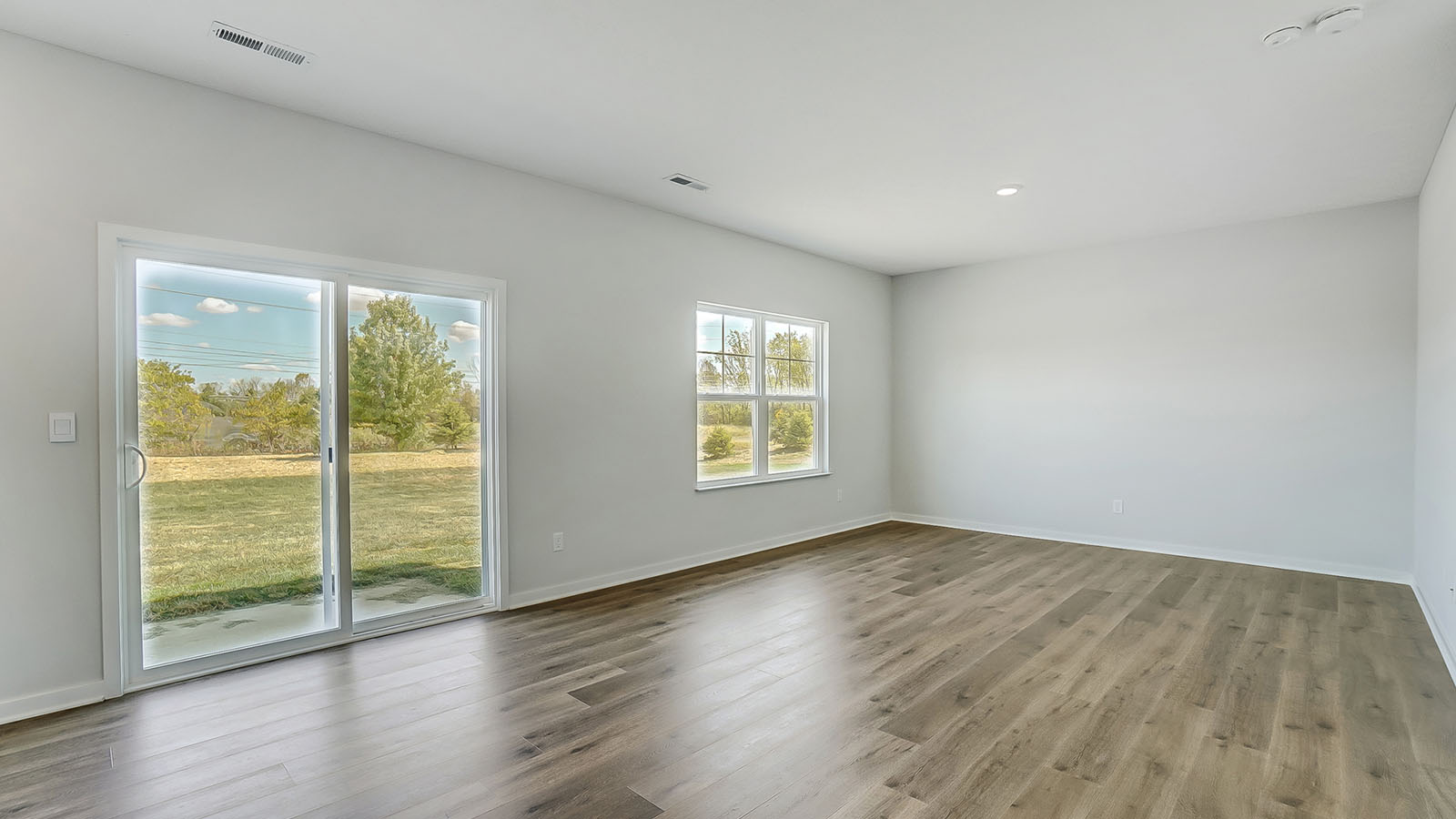 Spacious living room with brown flooring, white walls and windows
