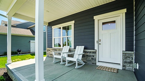 2-Store home with blue siding and stone watertable. Full porch with chairs.