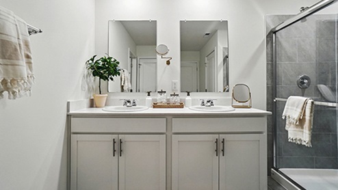 Primary bathroom with light gray cabinets featuring double sinks and mirrors