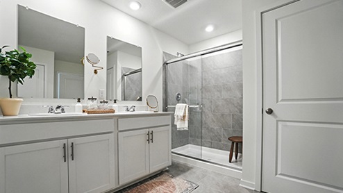 Primary bathroom with light gray cabinets featuring double sinks and mirrors