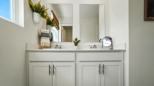 Bathroom with light gray cabinets featuring dual sinks and mirrors