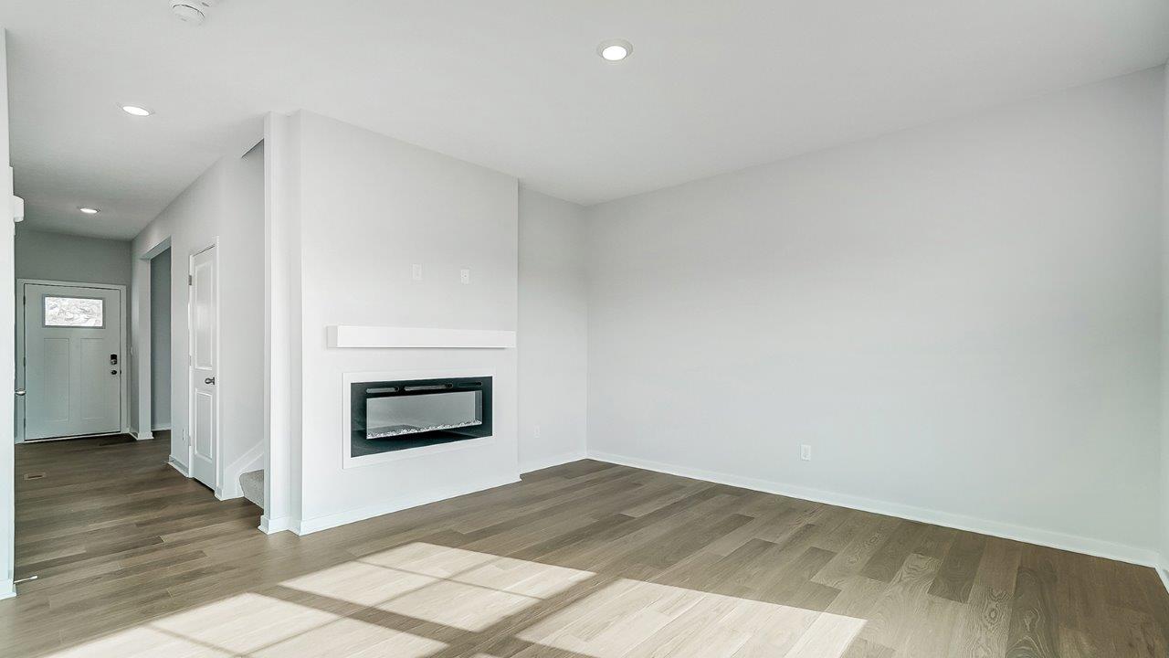Spacious living room with brown flooring, white walls, a black fireplace and windows