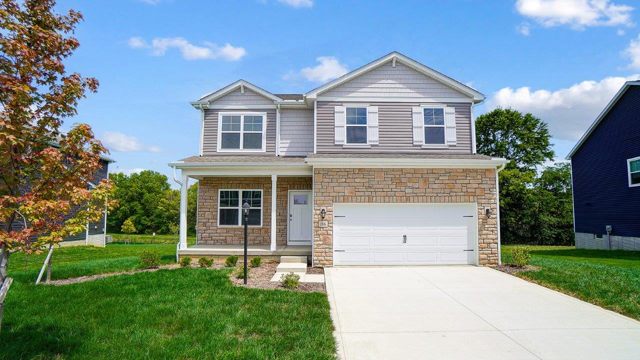 two story home with tan siding, partial stone front, covered front porch, two car garage