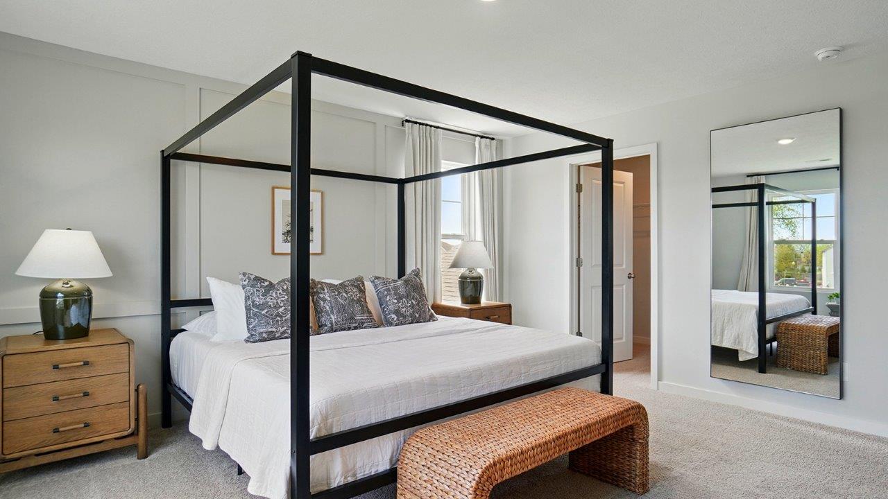 primary bedroom with a black canopy bed, night stands on either side and large windows