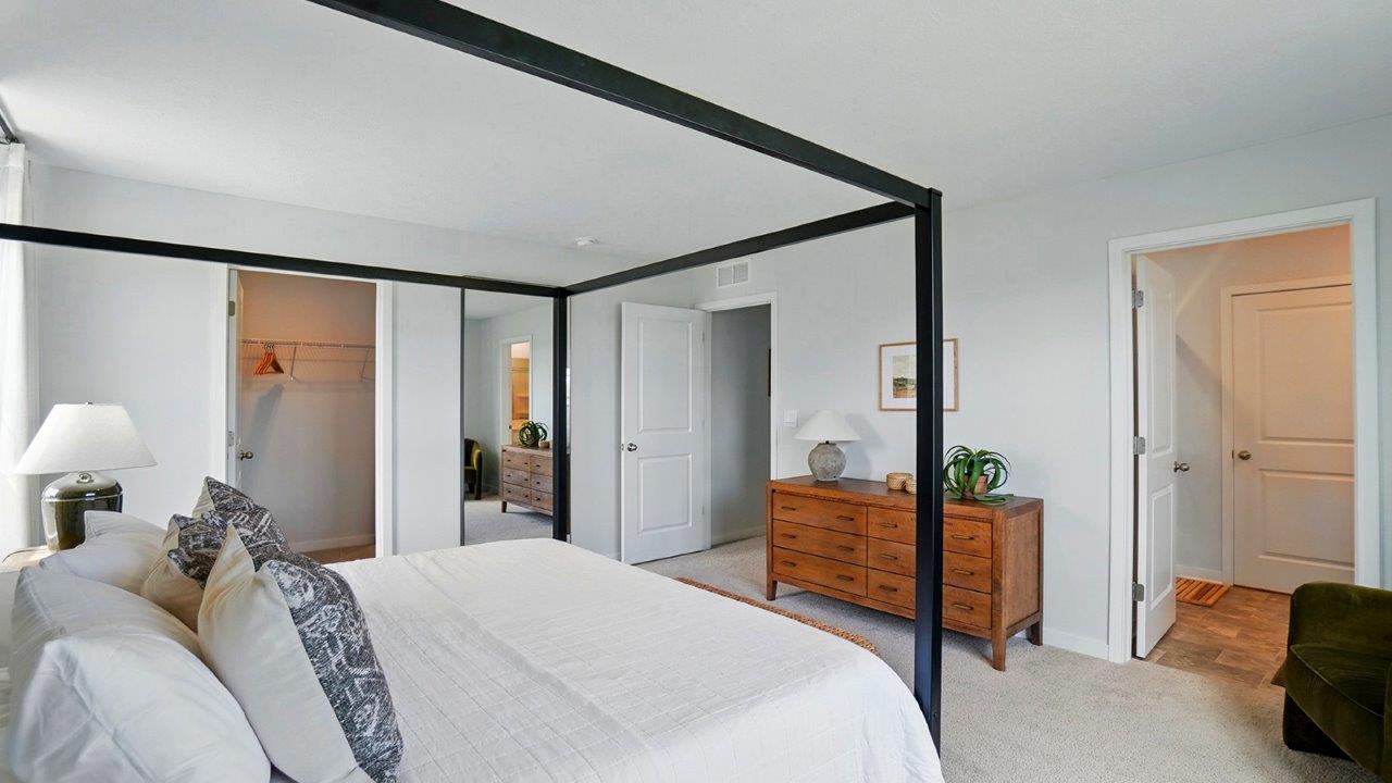 primary bedroom with a black canopy bed, night stands on either side and large windows