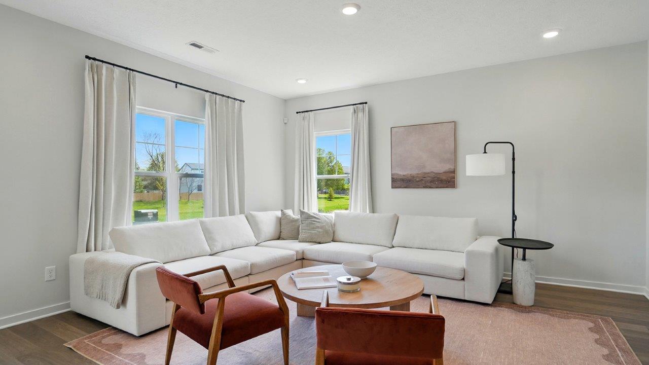 Living room featuring a white sectional against 2 windows, an orange rug and 2 red accent chairs