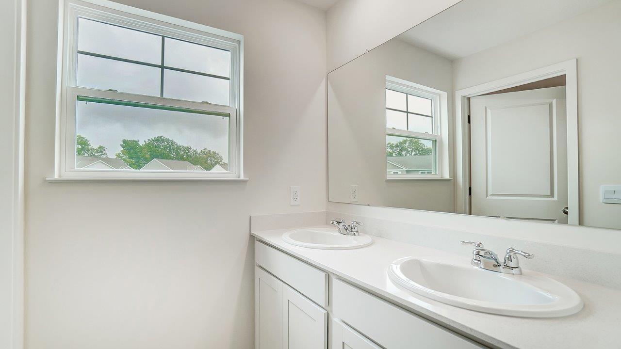 Bathroom with dual sinks and a wide mirror with a window.