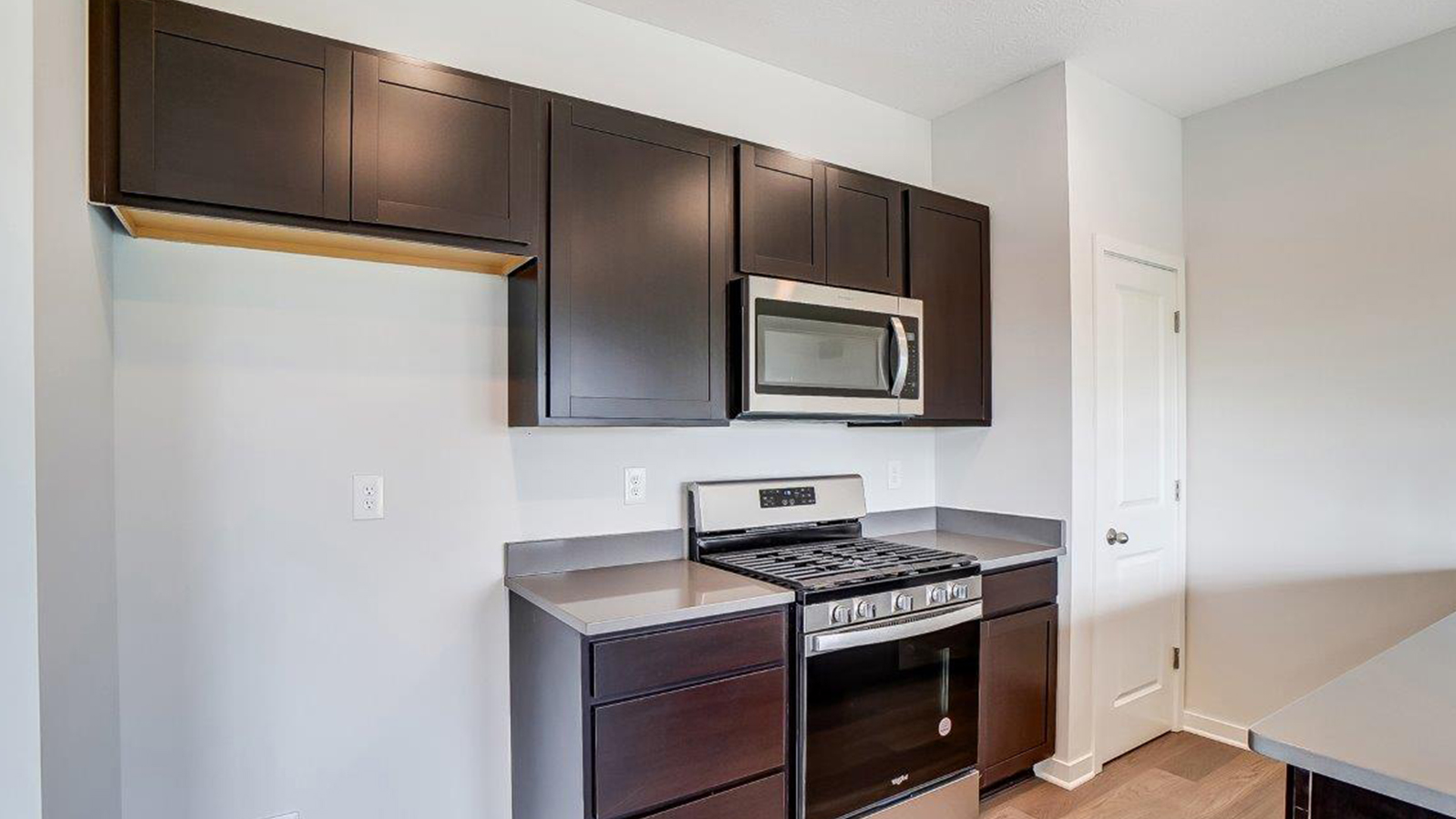 Kitchen featuring dark cabinets, new stainless steel appliances, and textured countertops.