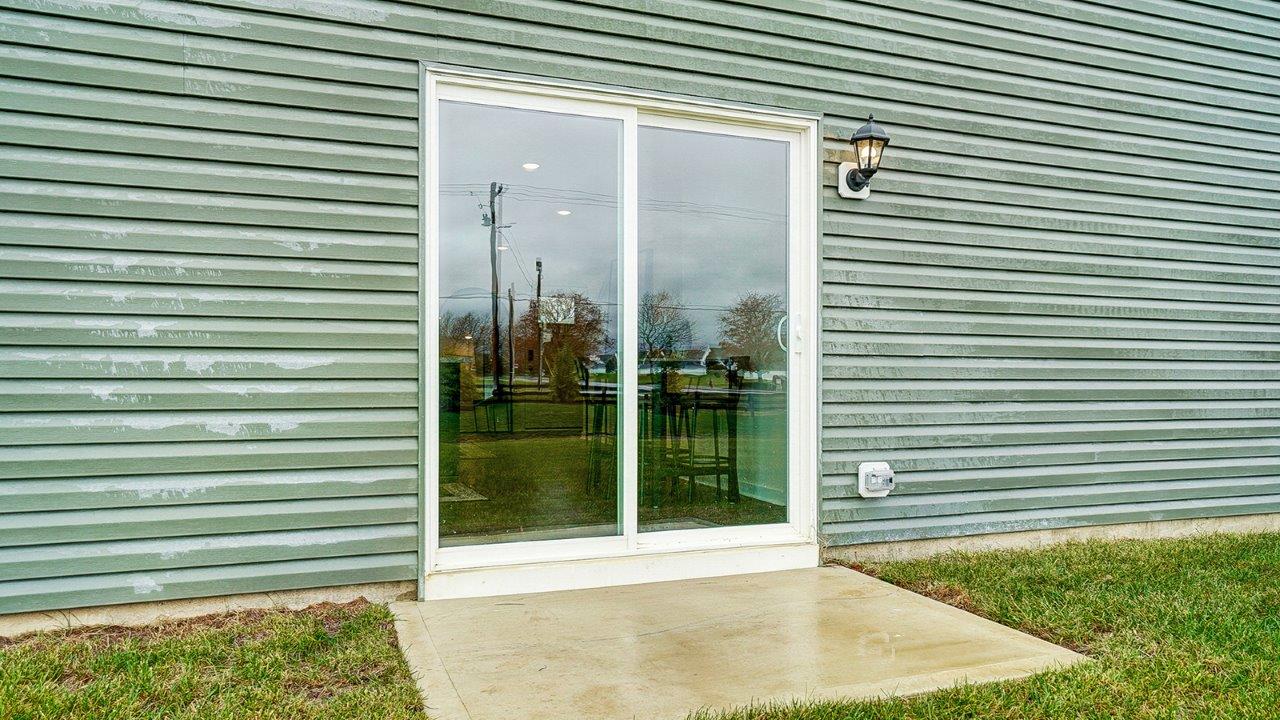 Sliding door with small patio and manicured lawn.