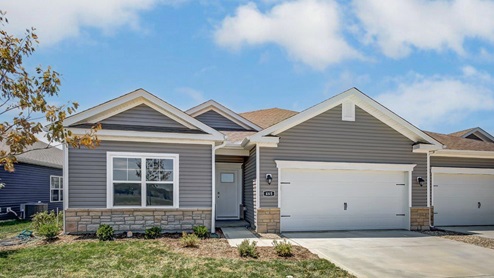 single story duplex with grey siding, stone water table, covered entry, two car garage