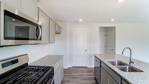 stainless steel microwave and range, grey cabinets, kitchen island, walk in pantry