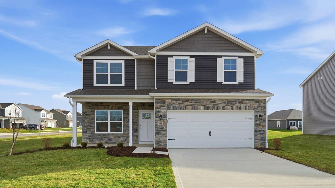 Two story home with grey siding, partial stone front, covered front porch and two car garage