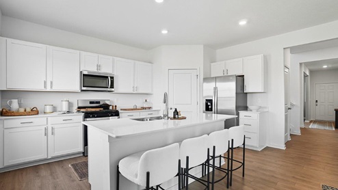 kitchen with white cabinets, built in island, corner walk in pantry, stainless steel appliances, foyer