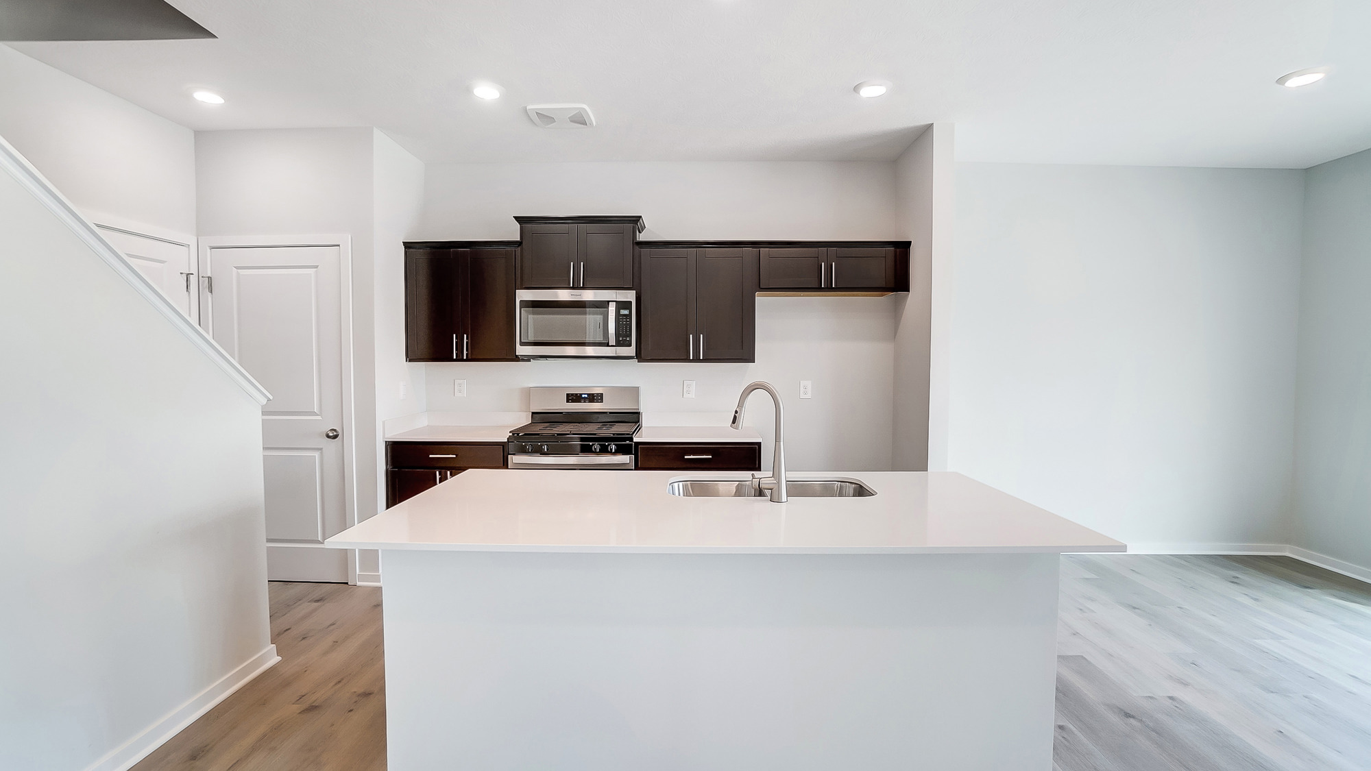 The kitchen has white countertops, ebony shaker-style cabinets, stainless steel appliances, and an island with a kitchen sink.
