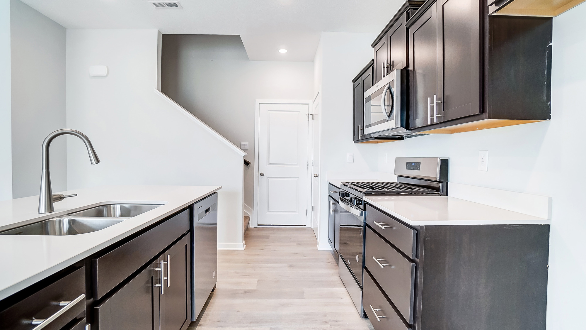 The kitchen has white countertops, ebony shaker-style cabinets, stainless steel appliances, and an island with a kitchen sink.