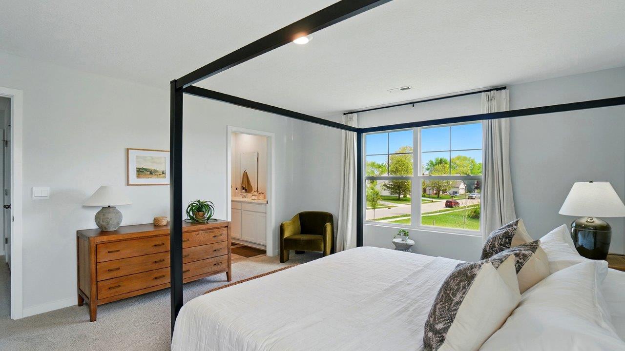 primary bedroom with a black canopy bed, night stands on either side and large windows