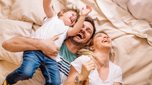 mother father and son laughing in bed