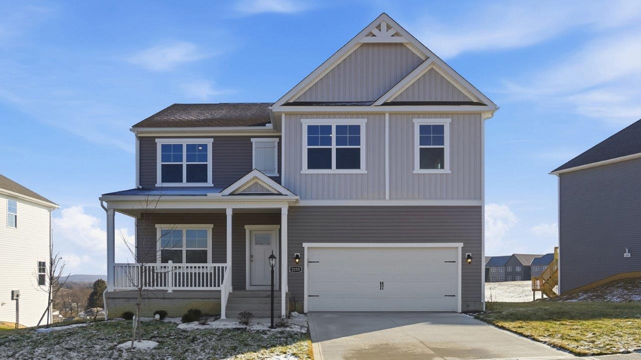 two story home with grey siding, covered front porch, partial stone front and two car garage