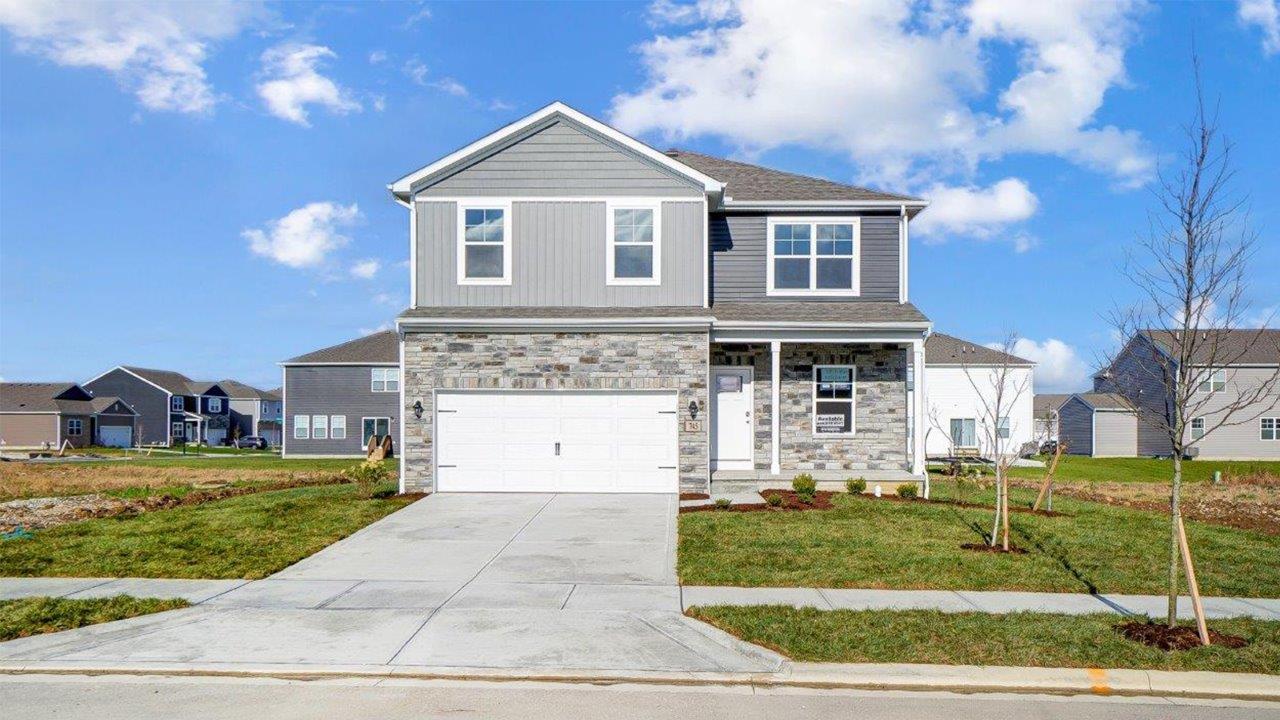 two story home with grey siding, partial stone front, covered porch, two car garag