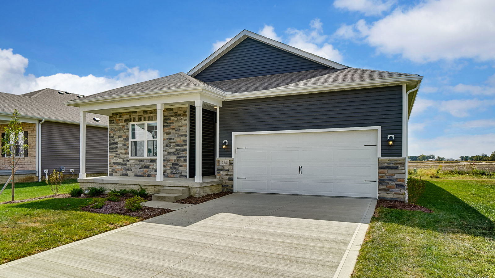 single story home with grey siding, partial stone front, covered front porch and two car garage