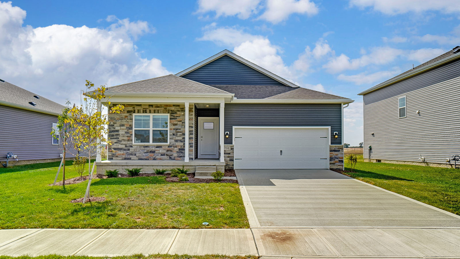 single story home with grey siding, partial stone front, covered front porch and two car garage