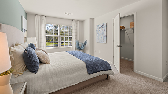 furnished primary bedroom with double window and walk in closet