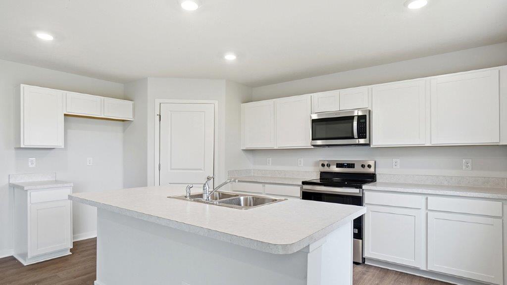 kitchen with white cabinets, built in island, stainless steel appliances, corner walk in pantry