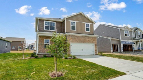 two story home with tan siding, partial stone, covered entry, two car garage angle