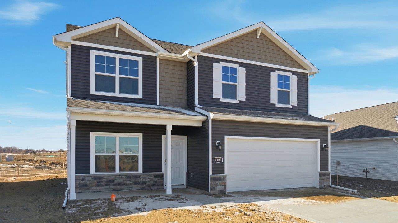 two story home with grey siding, stone water table, covered front porch and two car garage