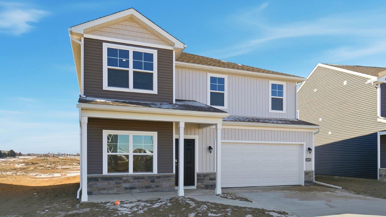 two story home with grey siding, stone water table, covered front porch and two car garage