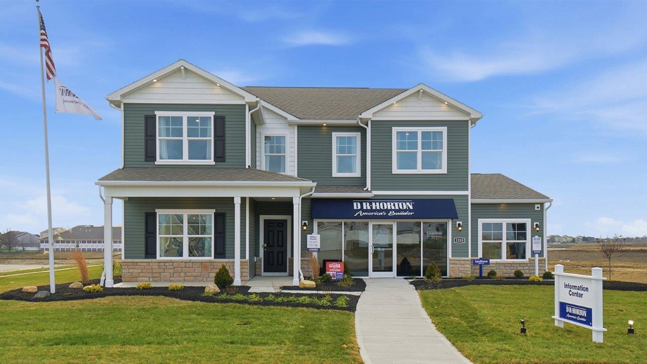 two story model home with green siding, covered front porch, three car garage and stone watertable