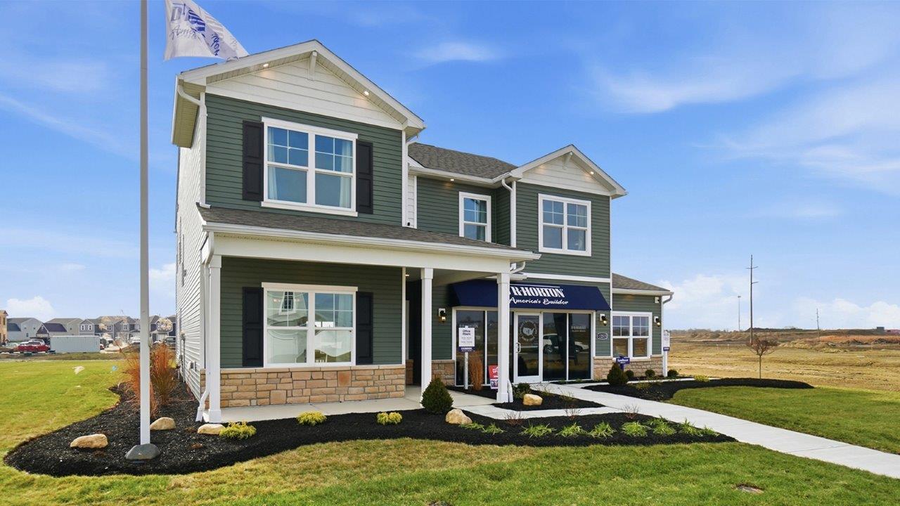 two story model home with green siding, covered front porch, three car garage and stone watertable