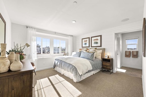 Amber Lynn Estates Plan 1547 Large spacious bedroom with wall bench in-front of side-by-side paned windows and full length curtains and entry to bathroom.