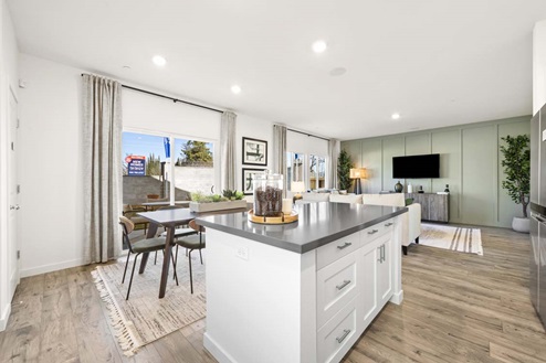 Open concept kitchen with island, gray countertops, and white cabinets, with view of living and dining area and sliding glass door.
