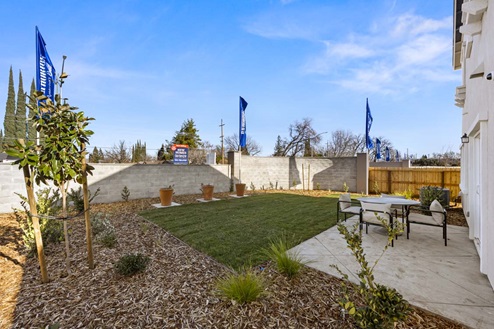Amber Lynn Estates Plan 1811 Backyard patio with lawn and landscaping, wooden fence, and concrete sound wall.