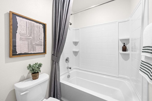 Toilet next to bathtub shower with built-in shelving and shower curtains.