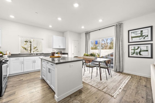 Kitchen island with gray countertops, white cabinets, dining area and sliding glass door.