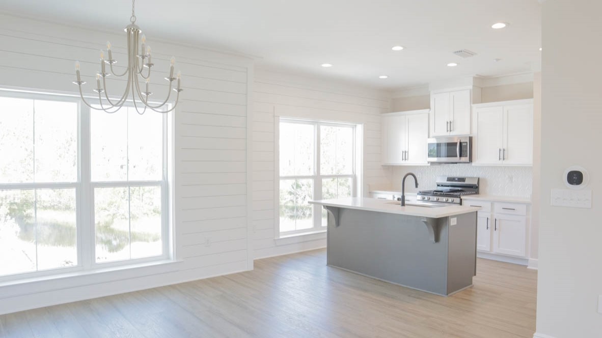 Dining and kitchen area with designer chandelier, large windows, and a shiplap accent wall.