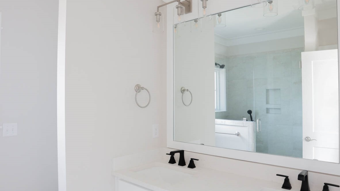 Primary bathroom with white cabinets, quartz countertops, and an enclosed glass shower with marbled tile.