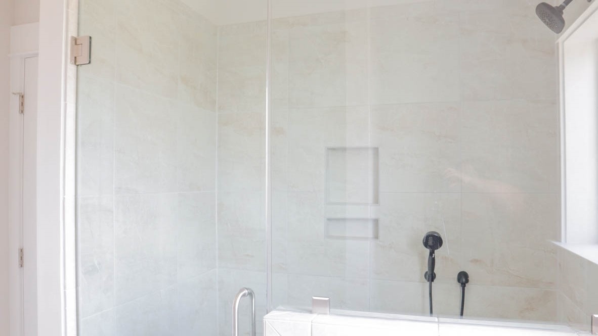 Enclosed shower with marbled tile and a glass door.